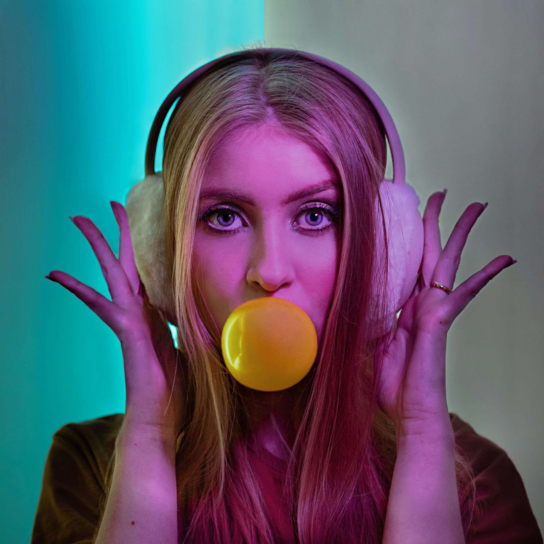 Woman wearing headphones blowing bubblegum against a colorful background