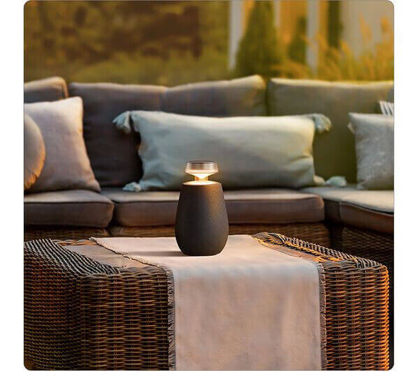 LG XBOOM 360 XO2 portable Bluetooth speaker on a table with soft seating in a cozy outdoor setting.