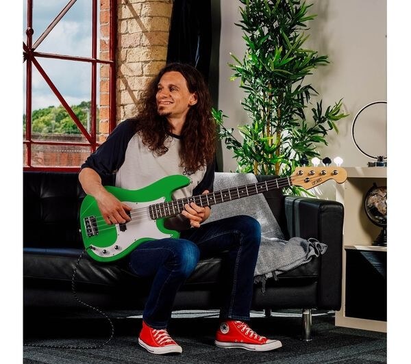 Person playing a 4/4 electric bass guitar bundle with amp in green color, sitting on a couch.