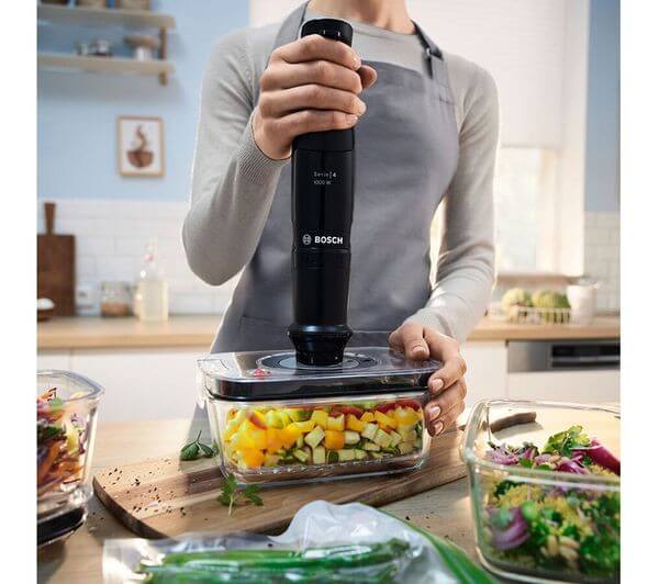 BOSCH SERIES 4 ErgoMaster MSM4B6V2GB HAND BLENDER VARIABLE SPEED 1000W BLACK in action with fresh vegetables in a kitchen.
