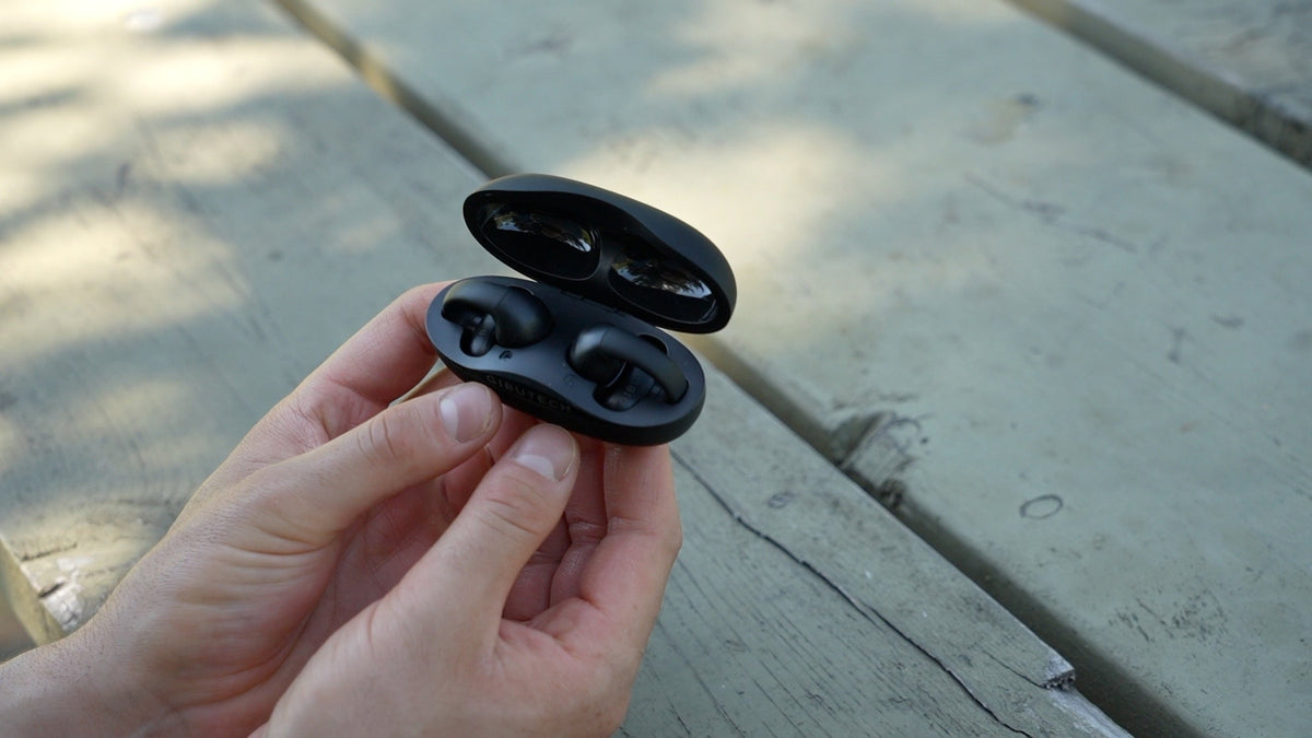 Gibutech Ultra Open Wireless Bone Conduction Earbuds with Dual Mic in charging case on a wooden surface.