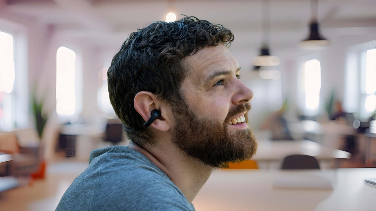 Man enjoying music with Gibutech Ultra Open bone conduction earbuds with dual mic in modern workspace.